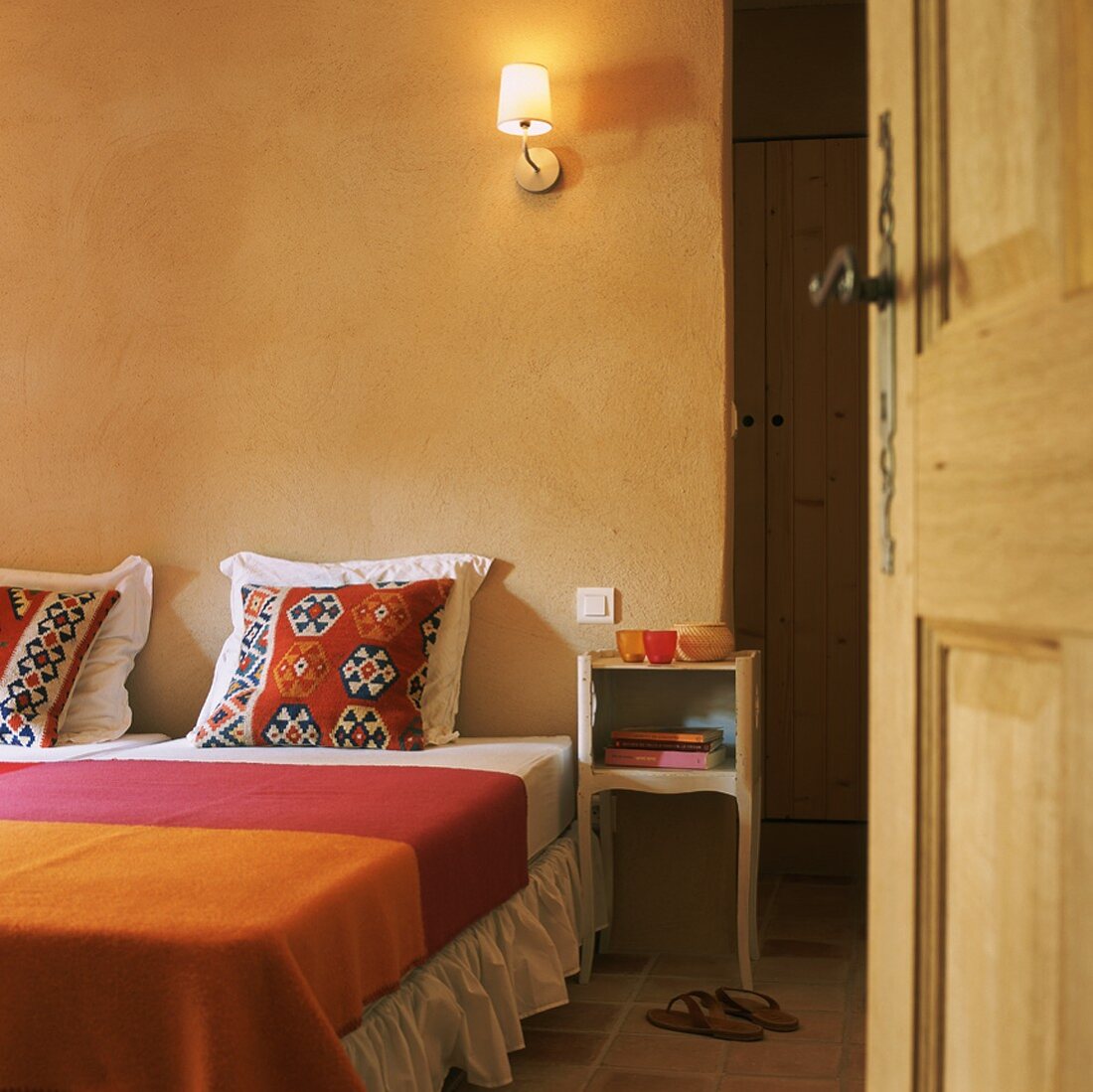 Schlafraum mit Terrakottafliesen, Doppelbett mit Ethnokissen und bunter Tagesdecke