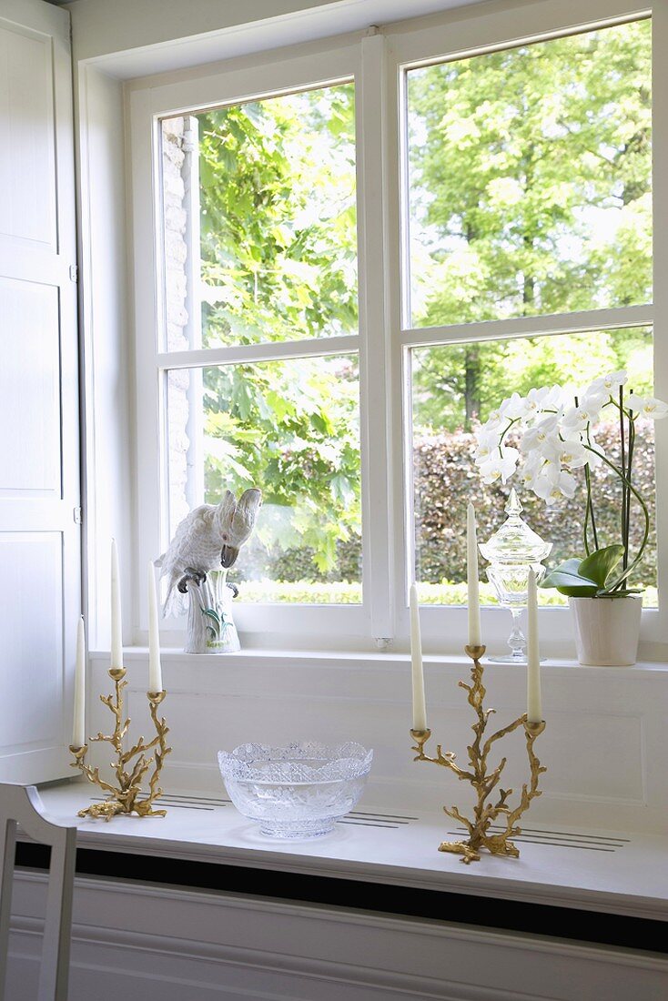 Sprossenfenster mit dekorativen Kerzenhaltern, Vogelfigur und Orchideentopf