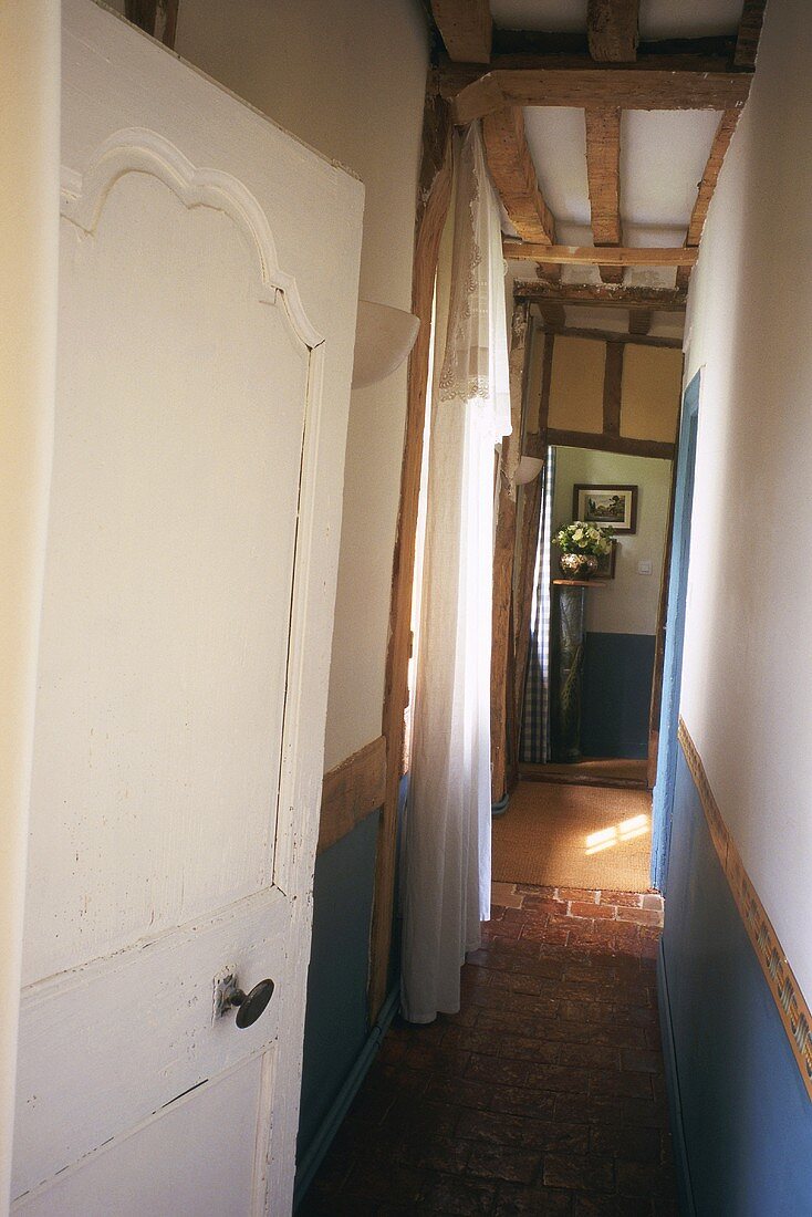 View along narrow hallway with wood-beamed ceiling and potted plant on pedestal in corner