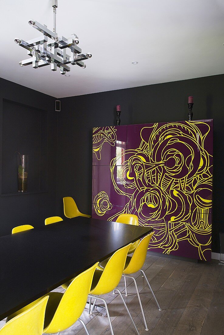 Wohnzimmer mit schwarzen Wänden, schwarzem Esstisch mit gelben Stühlen, originellem Schrank mit spiegelnder Fassade und Holzdielenboden