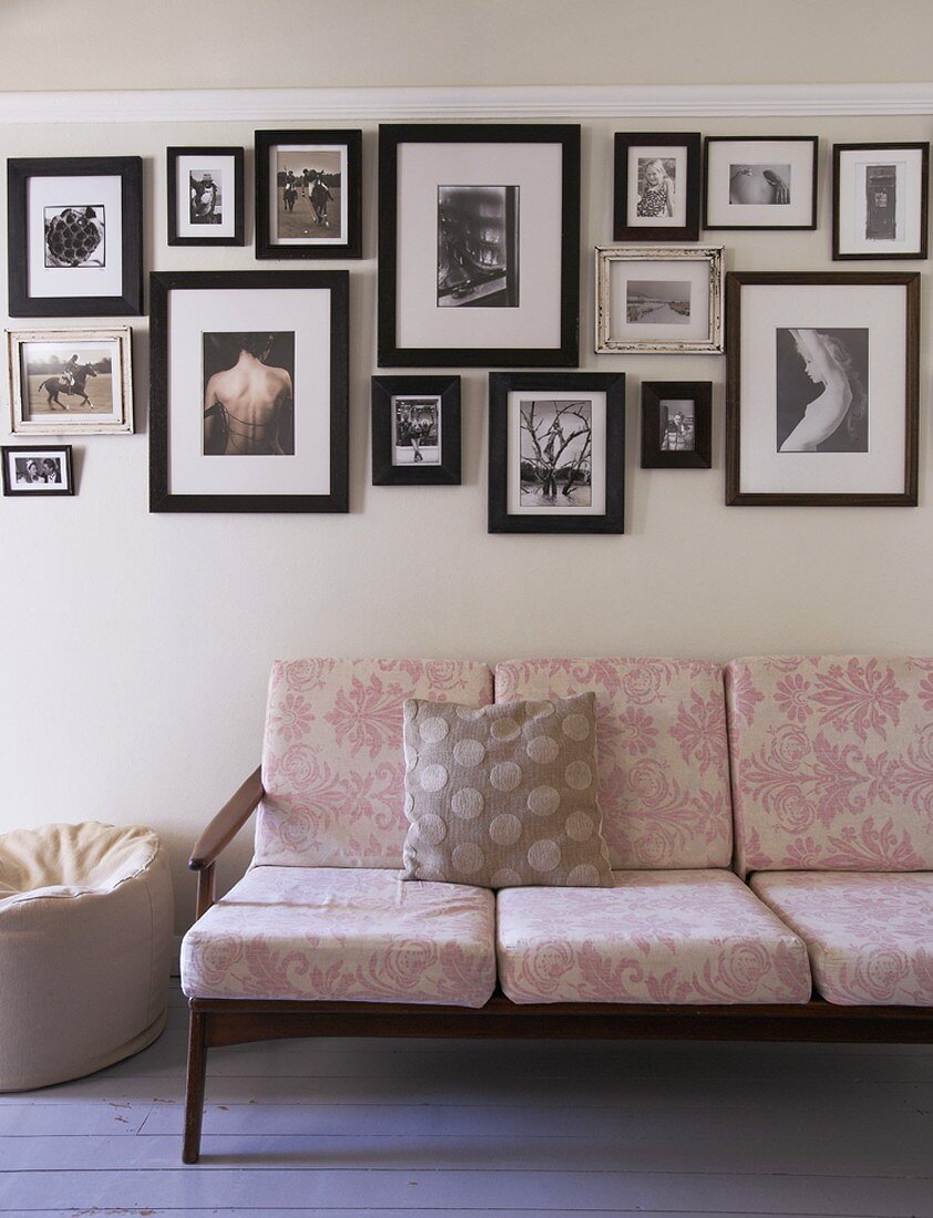 Collection of pictures in black frames on white wall above pink, floral sofa