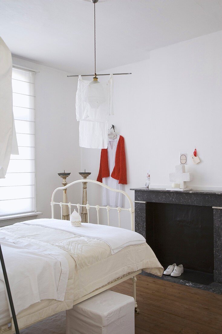 Bedroom with open fireplace, white vintage metal bed and unconventional pendant lamp with fabric lampshade