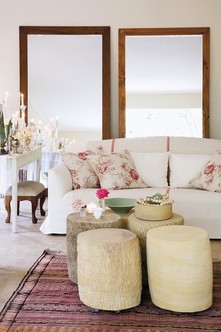 Zierkissen mit Rosenmotiv auf elegantem Sofa, davor fünf entrindete Baumstammtische