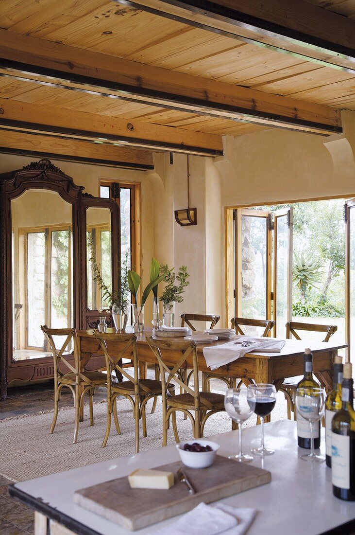 Lange Esstafel mit Stühlen vor Spiegelschrank und offener Tür zur Gartenterrasse