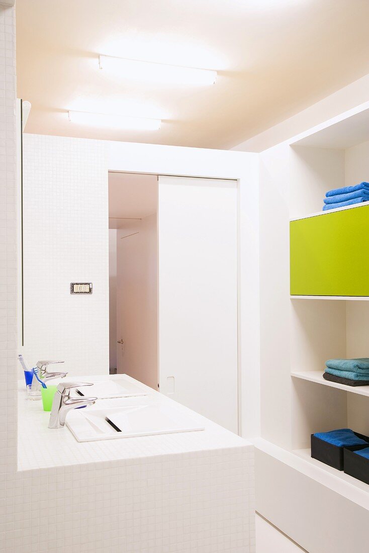 Weisses Badezimmer mit zwei Waschbecken und Regal mit blauen Handtüchern und grasgrüner Schranktür