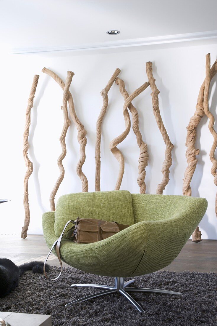 Green, upholstered swivel easy chair on soft, long-piled rug with decorative branches of gnarled wood in background