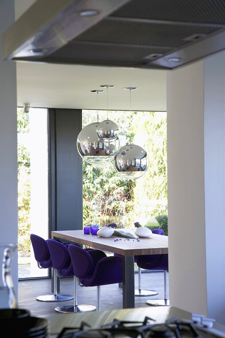 Dining room with floor-to-ceiling windows, dining table and swivel chairs; chrome, spherical pendant lamps suspended from ceiling