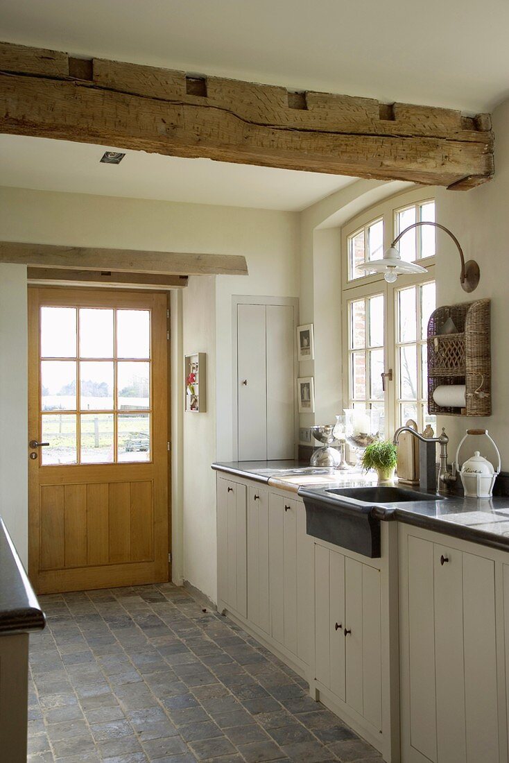 Küche mit Fenstertür, Terrakottafliesen und rustikalem Deckenbalken