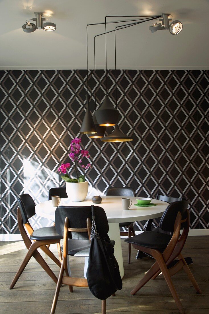 Round white dining table and black leather chairs in front of wallpaper with pattern of diamonds