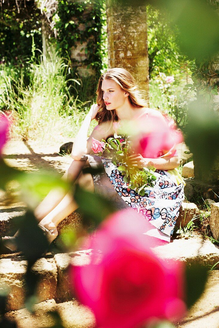 Junge Frau sitzt im Garten mit Rosen