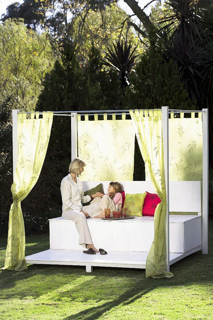 Mother and daughter sitting on day bed in garden