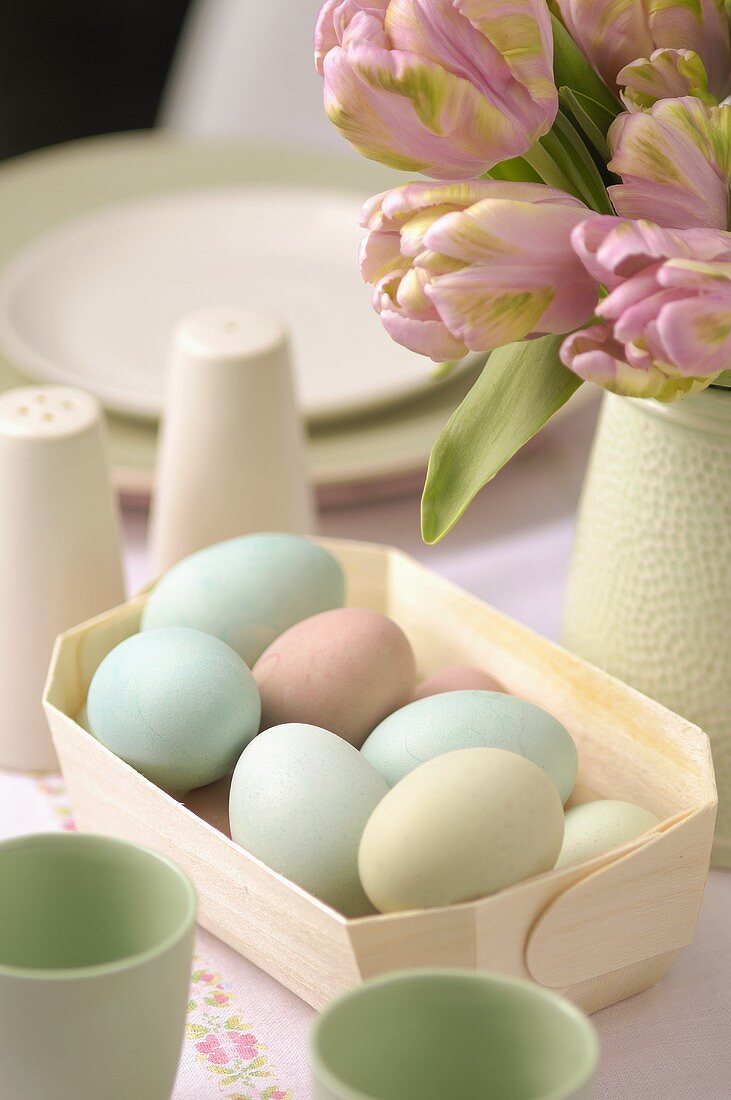 Coloured Easter eggs in a small basket with vase of tulips