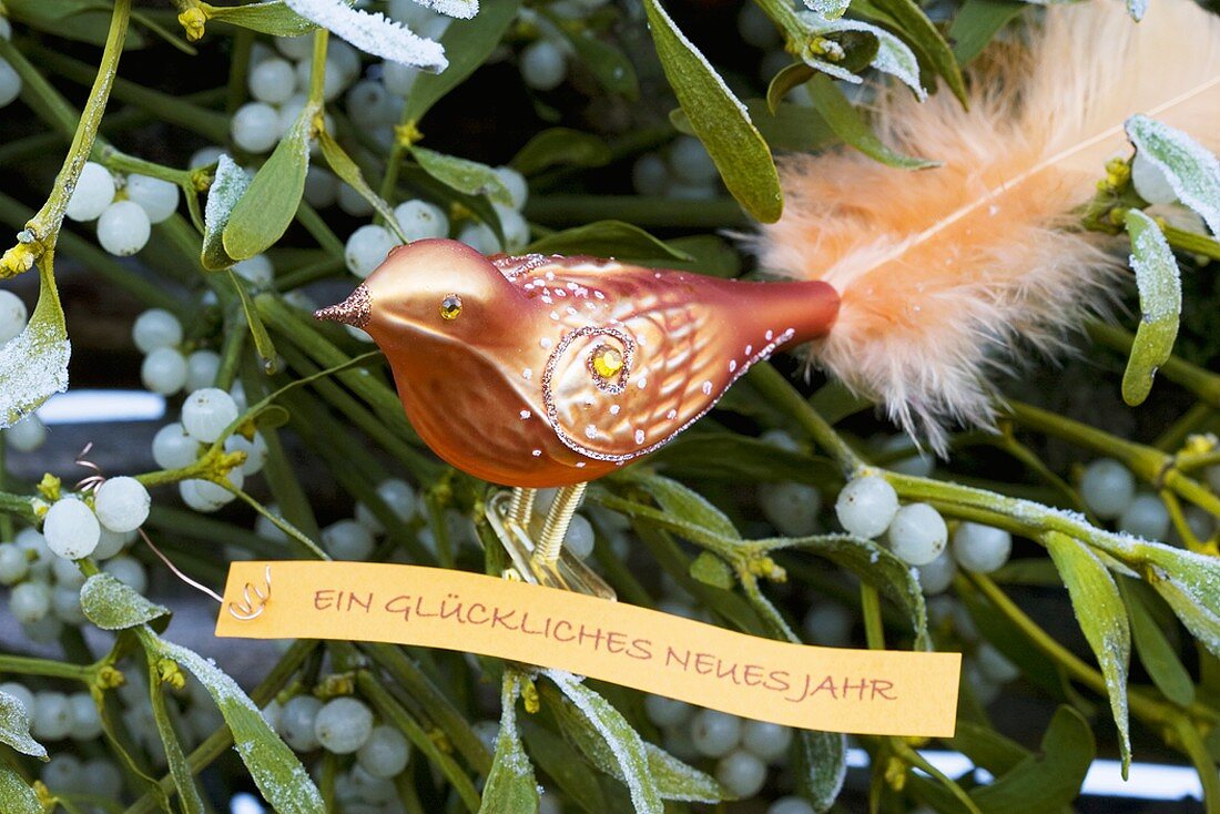 Glass bird with New Year greeting among mistletoe