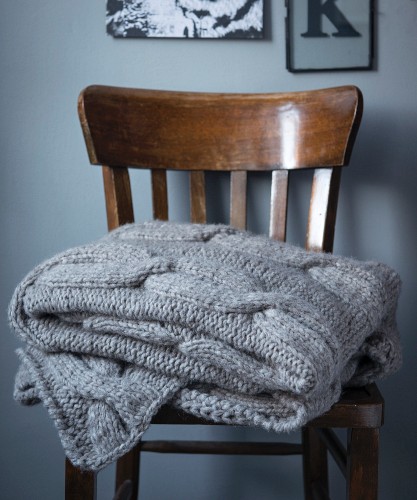 A grey blanket with a cable knit pattern on a wooden chair