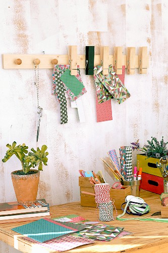 DIY-Wandleiste mit Möbelknöpfen und Holzklammern über Schreibtisch mit Bastelutensilien und Topfpflanze