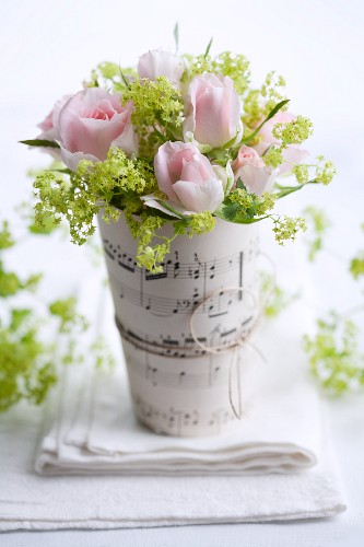 Posy of roses and elderflower in vase wrapped in sheet music