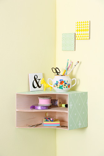 Small, wall-mounted, corner shelf unit made from box files covered in decorative paper