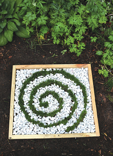 Miniature bed with a spiral of grass and white gravel decorating garden