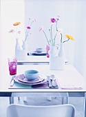 Pastel-coloured table setting  and vases of flowers on table