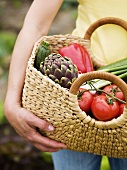 Frau hält Tasche mit frisch geerntetem Gemüse im Garten