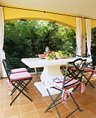 Various fruits on a stone table with a curved column foot and country house style chairs on a terrace