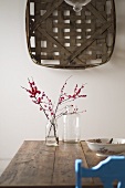 Woven basket on wall above twigs in glass jar on rustic wooden table