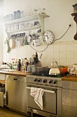 Kitchen counter with stainless steel cooker and dishwasher, station clock next to vintage shelving