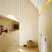 Ausgebautes Dachgeschoss mit weißer Holzverkleidung und halbhoher Schrank als Trennwand gegenüber maßgeschneiderten Einbauschränken