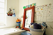 Korb und holzgerahmter Spiegel an der Badewanne, umgeben von Spielzeug und Kinderzeichnungen