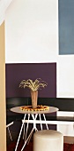 Kleiner, runder Tisch mit Eckbank und Polsterhocker vor grafisch bemalter Wand