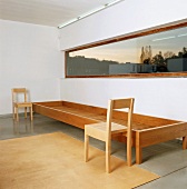 Zwei schlichte, moderne Holzstühle und ein langgestrecktes Holzgestell unter einem Fensterband