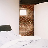 Altes Ziegelmauerwerk in Loftwohnung, Doppelbett mit Bad ensuite hinter runder, weisser Trennwand