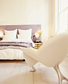 Doppelbett mit pastellviolettem Kopfteil und orgineller Sessel in hellem Schlafraum mit hoher Fensterfront