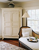 White, country-house-style cupboard and antique recamier with cane backrest in corner