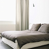 Minimalistischer Schlafraum in warmen Grautönen mit Doppelbett und Vorhang vor dem Fenster