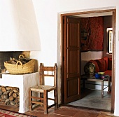 Weiß verputzter Kamin mit Holzvorräten und Blick in gemütlichen Wohnraum mit Kissen auf gemauertem Sofa