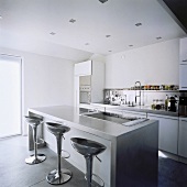 Moderne, offene Einbauküche mit verchromten Barhockern im Retrostil an einer Küchentheke