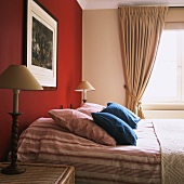 Schlafraum im Stilmix mit Doppelbett, bezogen mit bäuerlicher Bettwäsche und roter Wand mit gerahmtem Wandbild