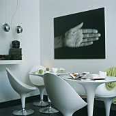 Moderne Wohnraumecke mit weissen Schalenstühlen, rundem Tisch und schwarz-weißem Fotobild an der Wand