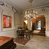Herrschaftlicher Arbeitsraum mit antikem Holztisch, Marmorfliesen, üppigem Kronleuchter und Gemälde mit Goldrahmen