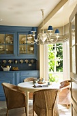 Freundliche Küche mit blauem Küchenbuffet, rundem, weissen Esstisch und Korbstühle