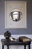 Animal horns and antique book on black console table below convex mirror