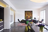 Open-plan interior with long dining table and lounge area with black butterfly chairs, couch and large painting of stag on wall