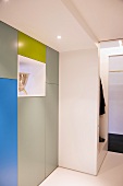 Fitted cupboards with smooth fronts in three colours and elegant metal vessel in opening