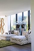 Comfortable chaise longues on soft rug next to flower arrangements and glass wall