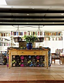 Simple wooden table with vase of flowers behind couch in living room with terracotta tiles and extensive, white bookcase