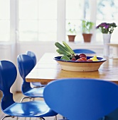 Tisch mit einer Obstschale und blauen Stühlen