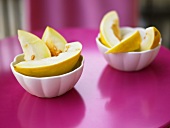 Melon slices in white bowls on a pink surface