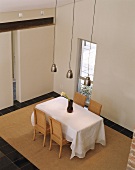 Blick von einer Galerie auf einen Esstisch mit weißer Tischdecke und Rattanstühle