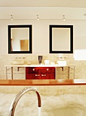 Eine mit Wasser eingelassene Badewanne aus Mosaikfliesen vor symmetrischen Waschtisch mit roten Schränken und große Wandspiegel